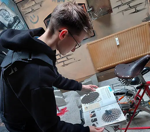 tatort_flensburg_02 Auf dem Bild ist ein Junge mit einer Brille, der ein Buch auf einem Fahrrad abgeleckt hat und dort etwas ließt.