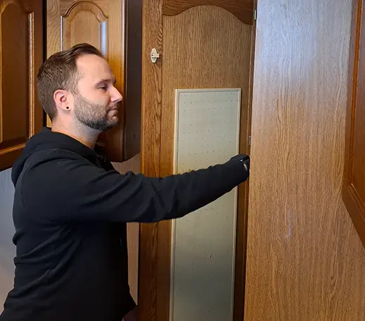 Ein Mann hat eine braune Schrankwand geöffnet und schaut hinein.