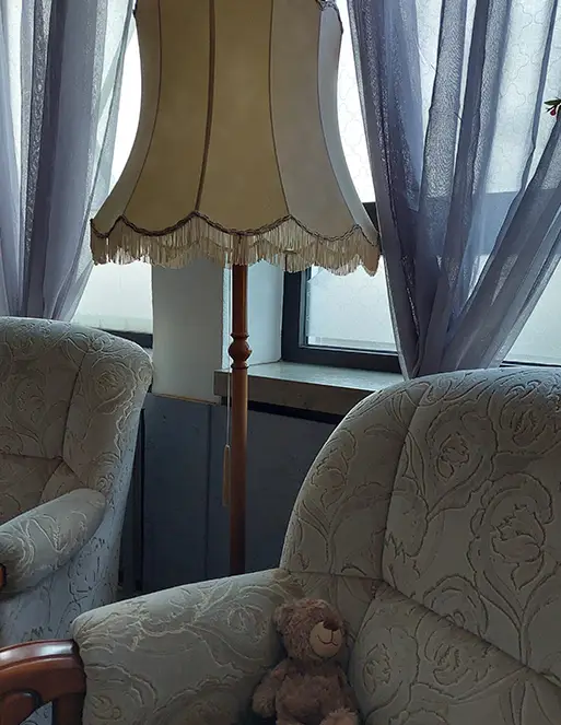 testament_flensburg_01 Auf dem Bild sind zwei Sessel. auf dem einem Sessel ist ein brauner Teddybär. Zwischen den Sesseln ist eine Stehlampe.